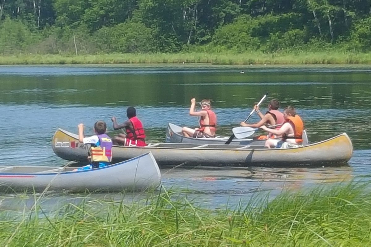 4 Scouts across three canoes canoeing on a still lake