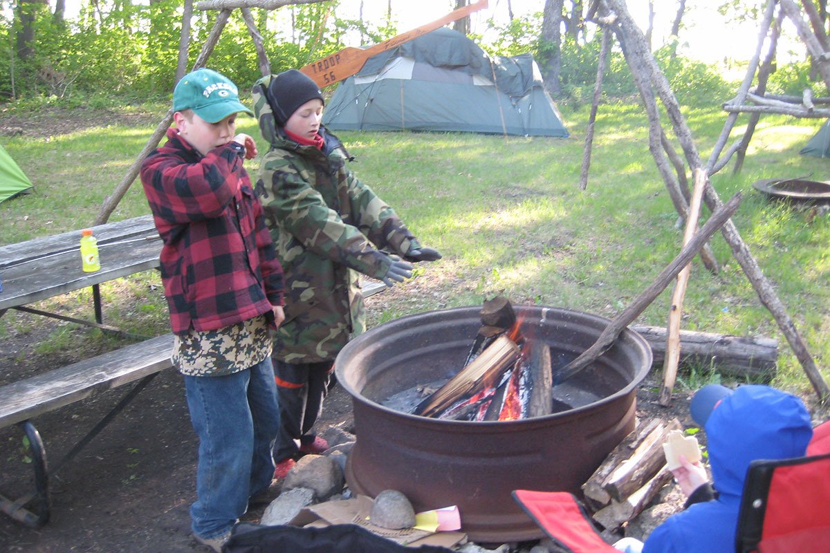 Two Scouts warming their hands as a fire burns in a metal fire pit
