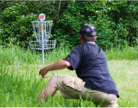 A man throwing a disc towards a disc golf hole surrounded by trees