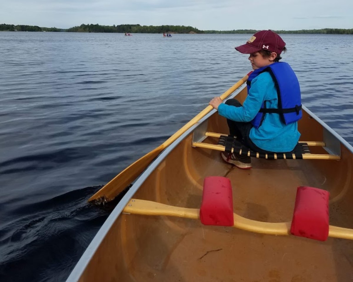 A young boy canoeing on a large lake, shoreline barely visible in the distance